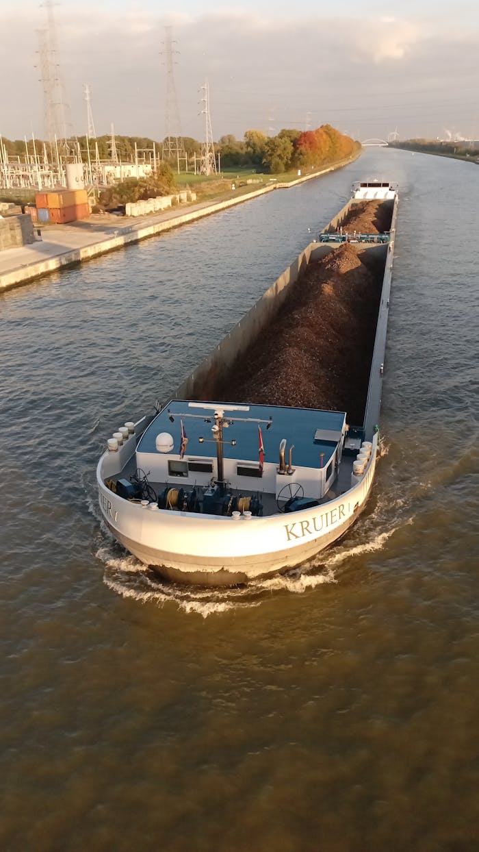 A cargo ship cruises through a canal during sunset, showcasing industrial shipping and transportation.